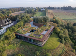 Wtopiona w ziemię bryła, dach porośnięty dziką roślinnością i naturalne bariery z nadrzecznych krzewów – ta realizacja to przykład projektowania, w którym architektura staje się częścią środowiska