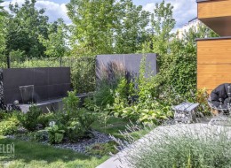 Oto nieduży ogród, w którym dużo się dzieje – w jego przestrzeni znajdziemy spory taras, kwitnące rabaty oraz przyciągający wzrok zbiornik ze ścianą wodną. 